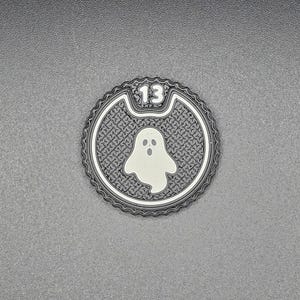 以下が含まれることがあります： ゴーストのグラフィックと数字の13が入った、白黒のハロウィーンをテーマにした円形のコースター。 コースターは、テクスチャード加工されたボーダーとパターン化されたインテリアを備え、灰色の背景に配置されています。