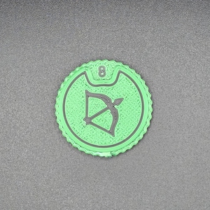 Puede incluir: Una ficha redonda verde claro con borde festoneado. La ficha presenta un diseño de arco y flecha negro y el número 8. El fondo es una superficie gris texturizada.