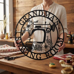 Peut inclure: Panneau en métal noir avec l'inscription "GRANDMA'S SEWING ROOM" entourant une machine à coudre et des motifs floraux. Le panneau est présenté devant un fond en bois, avec des fournitures de couture sur une table.
