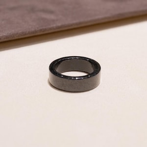 Puede incluir: Un anillo negro hecho de piedra pulida. El anillo es grueso y tiene una parte superior plana.