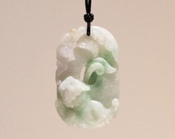 May include: A carved jade pendant with a black cord. The pendant features a light green and white design with flowing shapes. The jade is polished and has a smooth surface. The pendant is suspended against a neutral background.