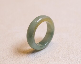 May include: A jade ring with a smooth, polished surface. The ring features a blend of green and yellow hues, creating a natural, organic appearance. The ring is a classic band style, suitable for everyday wear.