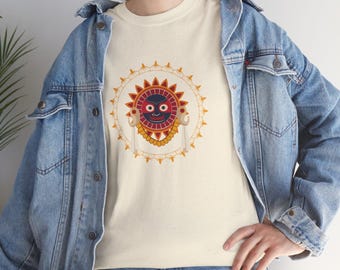 May include: Cream-coloured t-shirt featuring a sun-like graphic with a smiling face, red and yellow accents, and a decorative border. The design is centered on the shirt. The person is wearing a denim jacket.