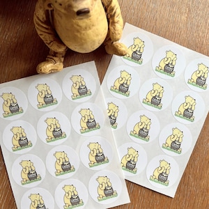 May include: Two sheets of white paper with round stickers featuring a cartoon Winnie the Pooh holding a pot of honey. The text "HONEY" is on the pot. The stickers are available in multiple sizes.