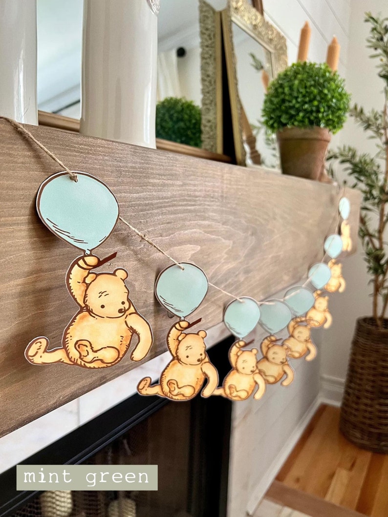 May include: A garland with a string of light blue balloons and brown teddy bears holding onto the balloons. The garland is hanging on a wooden mantel.