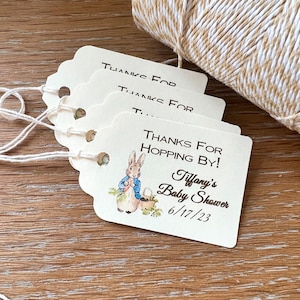 May include: Four white gift tags with scalloped edges and twine. The top tag says "Thanks for", the second tag says "Thanks for", the third tag is partially obscured, and the bottom tag says "Thanks for Hopping By! Tiffany's Baby Shower 6/17/23" and features a cartoon rabbit illustration.