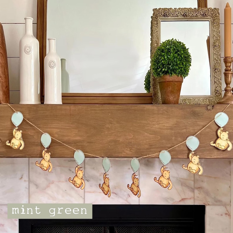 May include: A garland with a string of light blue balloons and Winnie the Pooh bears holding the balloons. The garland is hanging on a wooden mantel above a fireplace. The text "mint green" is written on the bottom of the image.