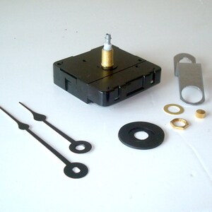 May include: Clock movement kit with black clock hands, a black plastic clock mechanism, and various metal hardware pieces. Includes a metal hanger, washers, and a brass nut. The clock hands are approximately 5 inches long.