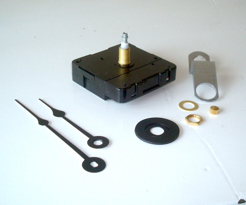 May include: Clock movement kit with black clock hands, a black plastic clock mechanism, and various metal hardware pieces. Includes a metal hanger, washers, and a brass nut. The clock hands are approximately 5 inches long.