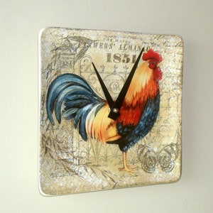 May include: A vintage-style clock featuring a rooster with a red comb and blue tail feathers. The clock face is surrounded by a decorative border with the text "The Farmers' Almanac 1851".