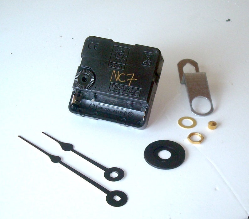May include: A black quartz clock movement with the text "NC7" and various clock-making components. Includes a metal hanger, washers, a nut, and black clock hands. The clock hands are approximately 5 inches long.