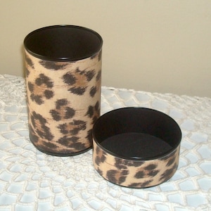 May include: Two round containers with a leopard print design. The containers are made of cardboard and have a black interior.
