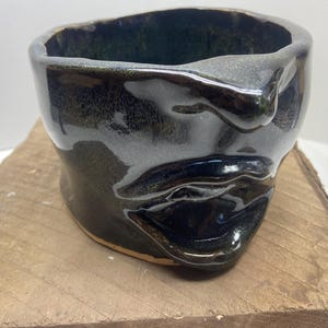 May include: A dark green ceramic planter shaped like a face with a wide mouth and a prominent nose.