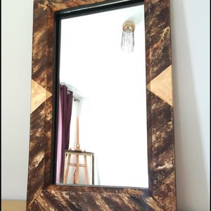 Peut inclure: Miroir rectangulaire avec un cadre décoratif en bois. Le cadre présente un motif marbré marron et doré avec un cadre intérieur noir. Le haut du cadre est incurvé et les coins ont des accents dorés.