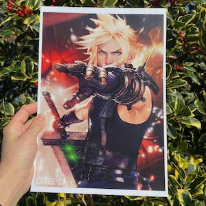 May include: A print depicting a character with spiky blonde hair and blue eyes, holding a large sword. The character is wearing black armour and is reaching towards the viewer. The word "SCATTERED" is printed at the bottom.