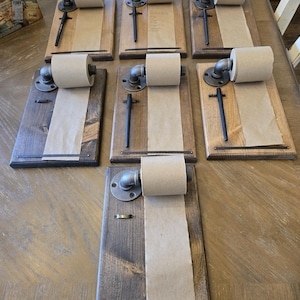 May include: Seven wooden memo boards with a brown stain finish. Each board has a metal pipe fitting with a roll of brown paper attached. A black metal pen is attached to each board.