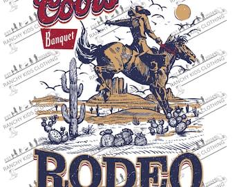 May include: Graphic tee design featuring a rodeo scene with a cowboy riding a bucking horse. The design includes the text "Coors Banquet" and "RODEO" in a vintage style, with a desert landscape background.