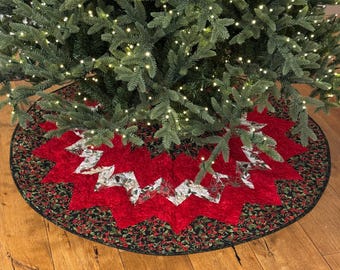 May include: A red and green Christmas tree skirt with a starburst design. The skirt is made of fabric and has a black border.