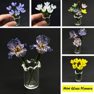 Puede incluir: Surtido de mini flores de vidrio en varios colores, incluyendo morado, blanco, amarillo y rosa. Cada flor se muestra en un jarrón de vidrio transparente con borde rizado.