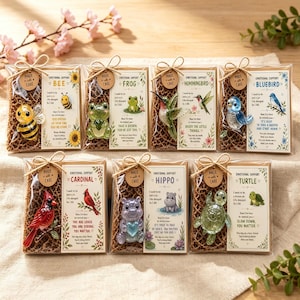 May include: Seven individual clear plastic gift sets, each containing a small glass animal figurine and a printed card. The animals include a bee, frog, hummingbird, bluebird, cardinal, hippo, and turtle. Each set features a brown twine bow and a small circular tag labelled Made with care.