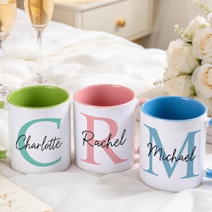 May include: Three white ceramic mugs with colored interiors and handles. The first mug has a green interior and handle with a large letter C and the name Charlotte. The second has a pink interior and handle with a large letter R and the name Rachel. The third has a blue interior and handle with a large letter M and the name Michael.