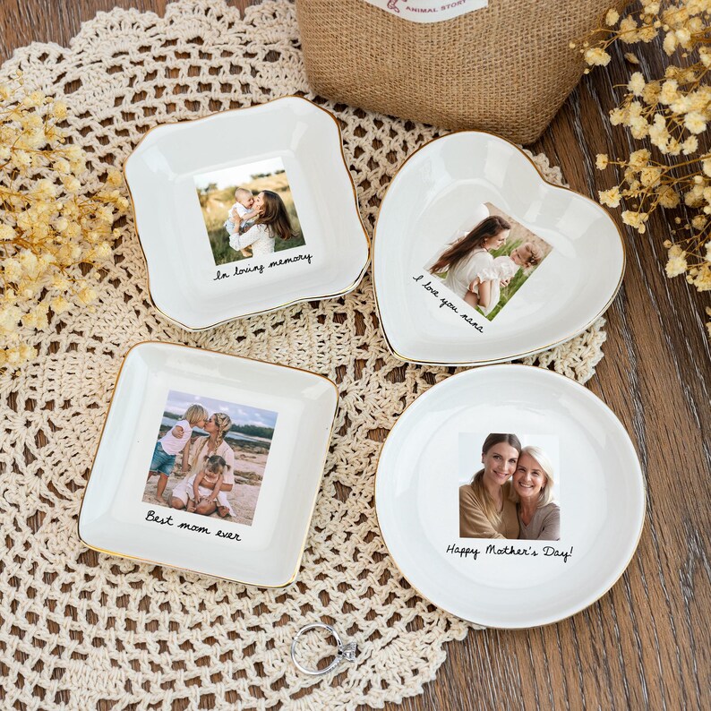 May include: Four white ceramic dishes with gold trim, each featuring a photograph and a handwritten message. The shapes include a square, a heart, and a circle. Messages include "In loving memory," "I love you nana," "Best mom ever," and "Happy Mother's Day!"