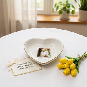 May include: A heart-shaped, white ceramic dish with a gold rim, featuring a photo and the words "I love you nana." A card with a bow reads "To my special Nana, a little something to keep close to your heart." Yellow tulips are arranged nearby.