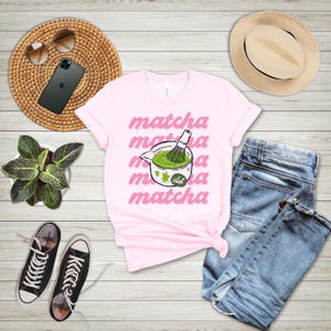 Pink matcha club shirt flat lay with bold matcha design, cute tea lover graphic tee for cafe girls and cozy casual outfits.
