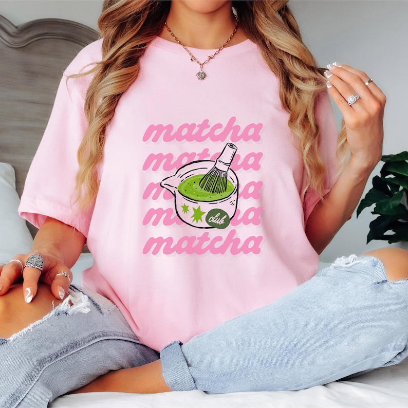 Pink matcha club shirt with green matcha drink graphic and repeated pink lettering, trendy tea lover graphic tee for women.