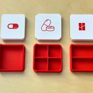 May include: Three white pillbox lids with red icons of pills and a red pillbox base. The pillbox bases are red and have different compartment configurations. The pillbox is designed to hold pills and medications.