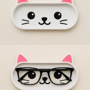 Könnte beinhalten: Zwei weiße, katzenförmige Tabletts mit rosa Ohrakzenten. Ein Tablett ist leer, das andere enthält eine Brille mit schwarzem Rahmen. Die Tabletts haben schwarze Gesichtsmerkmale, einschließlich Augen, Nasen und Schnurrhaare. Die Tabletts sind für kleine Gegenstände konzipiert.
