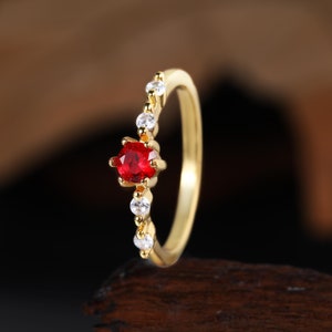 May include: A gold ring with a single red gemstone and a row of smaller white gemstones.