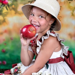 May include: A young person wearing a straw hat and a white dress with red accents, holding a red apple. The dress has a vintage apple print. The background features an apple tree with red apples.