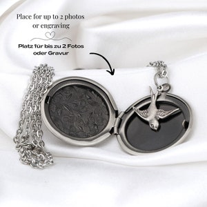 May include: A silver-toned locket necklace with an oval pendant and a small bird charm. The locket opens to reveal space for photos or engraving. The text "Place for up to 2 photos or engraving" is visible.
