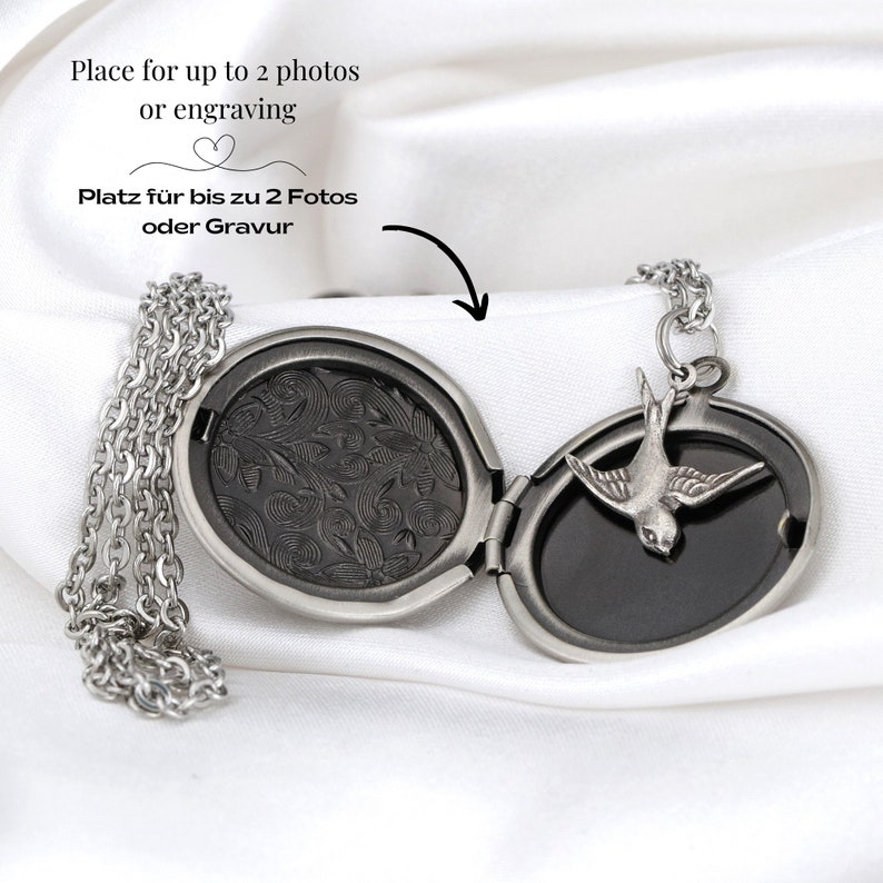 May include: A silver-toned locket necklace with an oval pendant and a small bird charm. The locket opens to reveal space for photos or engraving. The text "Place for up to 2 photos or engraving" is visible.