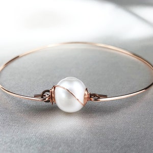 Peut inclure: Un bracelet fin en or rose avec une seule perle blanche enroulée de fil.