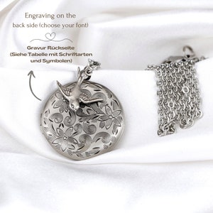 May include: A silver-toned locket necklace with a bird and floral design. The round locket features engraved flowers and swirls, with a bird perched on top. The chain is also silver-toned. Text on the image says, "Engraving on the back side (choose your font)".