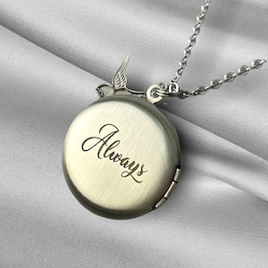 May include: A silver-toned locket necklace with a round pendant engraved with the word "Always" in cursive script. A small bird figure adorns the top of the locket. The necklace chain is also silver-toned.
