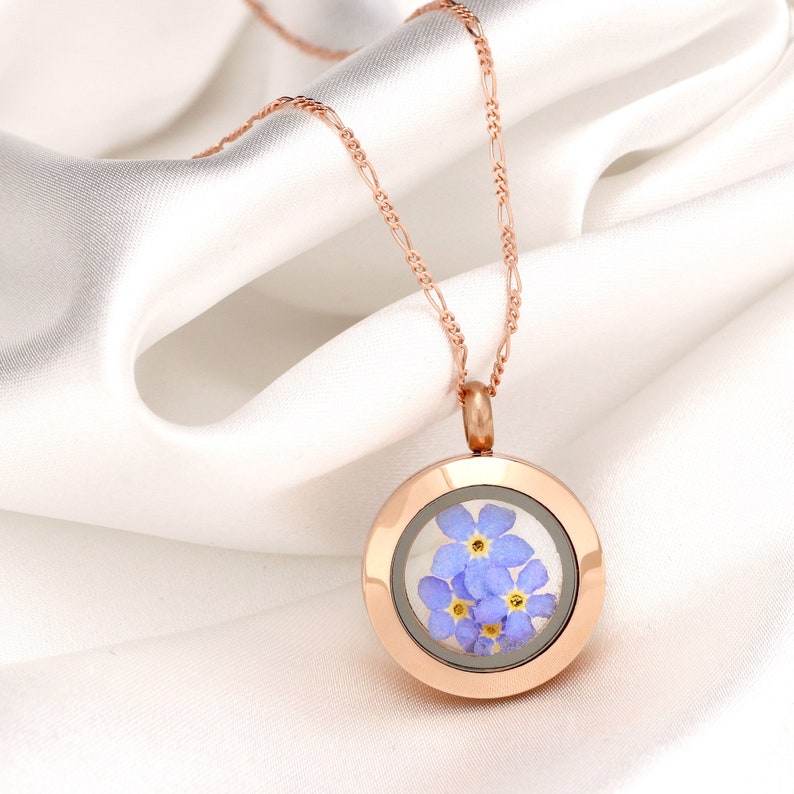 Puede incluir: Un collar de oro rosa con un colgante redondo en forma de medall&oacute;n con un dise&ntilde;o de flores de nomeolvides prensadas.