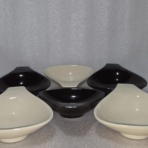 May include: A collection of six ceramic bowls in a variety of colors. The bowls are in black and off-white. The bowls have a unique, asymmetrical shape, with a wide, shallow bowl and a slightly raised base. The bowls are arranged in a group.