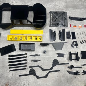 May include: A disassembled black and yellow model car kit, with various parts including the chassis, body, and suspension components. The kit includes screws and other small parts, arranged on a gray surface.