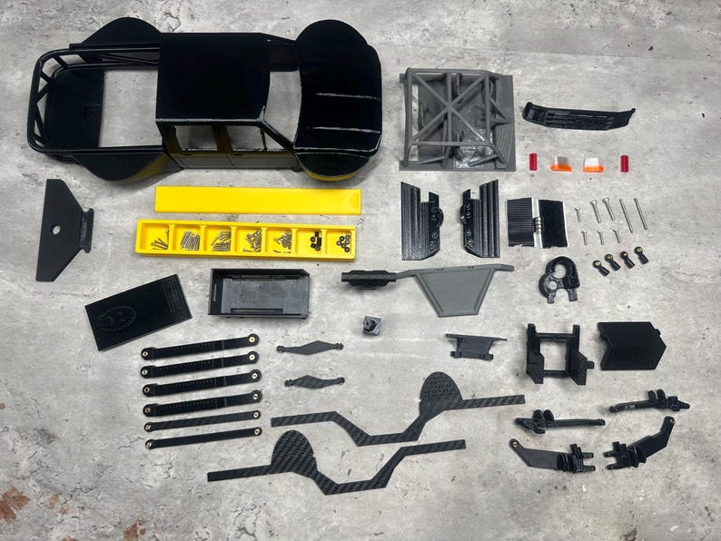 May include: A disassembled black and yellow model car kit, with various parts including the chassis, body, and suspension components. The kit includes screws and other small parts, arranged on a gray surface.