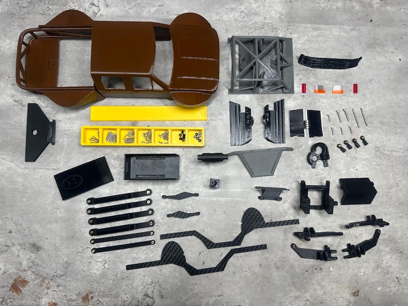 May include: A disassembled model car kit with various components. The brown body and roll cage are visible, along with gray and black parts, screws, and a yellow tray. The parts are arranged on a gray surface.
