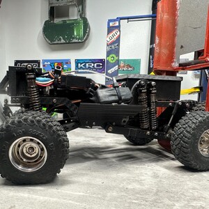 May include: Black and silver remote control truck with large, knobby tires. The truck has a black chassis, visible suspension, and a red body component. The tires are marked with "1.0" and "55x22".