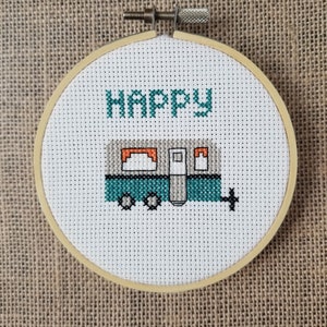 May include: A white cross-stitch embroidery hoop with a teal camper van and the word "Happy" stitched in green thread.