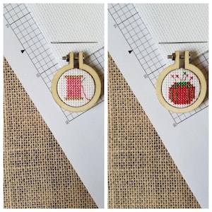 May include: Two small wooden embroidery hoops with cross-stitch designs. The hoop on the left has a pink spool of thread with a needle. The hoop on the right has a red and green Christmas present with a bow.