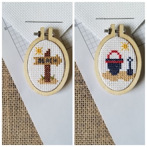 May include: Two small wooden embroidery hoops with cross-stitch designs. The first hoop features a wooden signpost with the word "BEACH" on it. The second hoop features a red and blue sailboat with a yellow sun and an anchor.