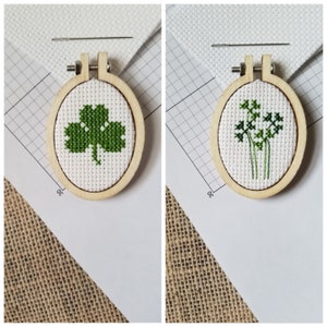 Peut inclure: Deux petits cerceaux à broder en bois avec un tissu blanc et une broderie verte. Un cerceau présente un motif de trèfle et l'autre une brindille de feuilles vertes.