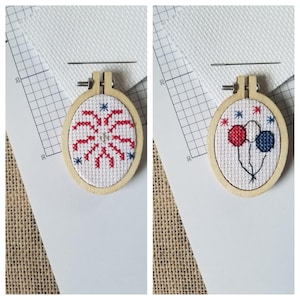 May include: Two small, oval-shaped cross-stitch hoops with wooden frames. One features a red and blue firework design, the other has red and blue balloons. Both are on white fabric, with a grid background and a burlap surface.