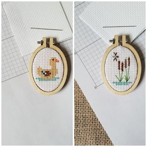 May include: Two embroidery hoop ornaments. One features a brown duck on a blue background. The other features brown reeds on a blue background.